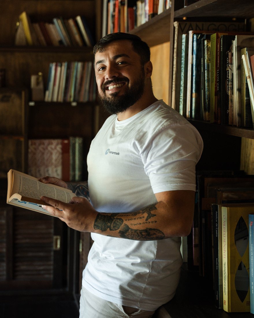Júlio Gonçalves sorrindo com um livro na mão, em frente a uma estante
